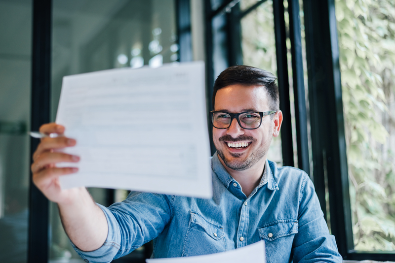 Portrait of young smiling cheerful man entrepreneur or businessman in casual office working with charts and graphs looking at